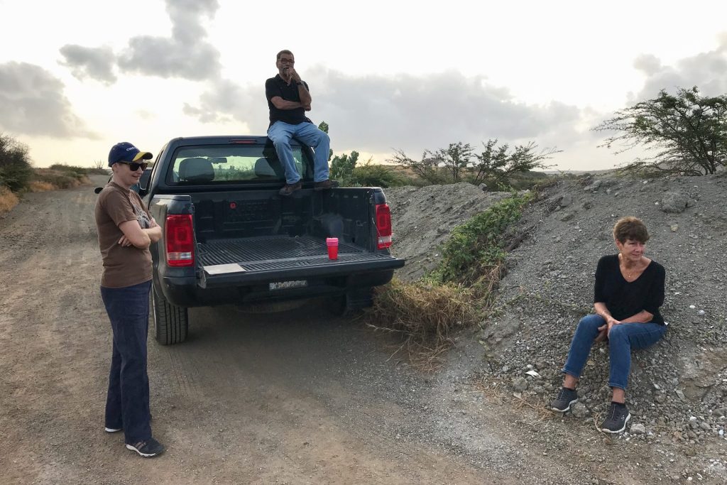 two people are in front of a car en one is sitting on the car